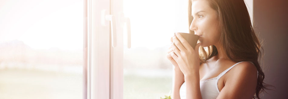 10 Tipps für Morgenmuffel: Eine Frau trinkt Kaffee am Fenster