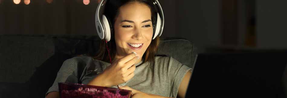 beste Serien der letzten Jahre: junge Frau sitzt mit Kopfhörern und Popcorn vor Laptop