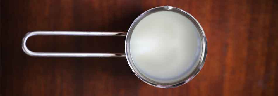 Warum kocht Milch so schnell über? Ein Topf mit Milch steht auf Holz