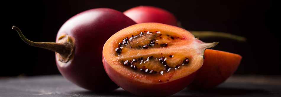 Eine Tamarillo liegt neben einer aufgeschnittenen Frucht