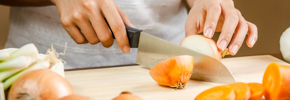 Eine Frau schneidet mit einem großen Messer eine Zwiebel in Hälften