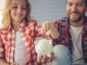 Neu ab 2020: mehr Kindergeld, ein Mädchen steckt Geld in ein Sparschwein