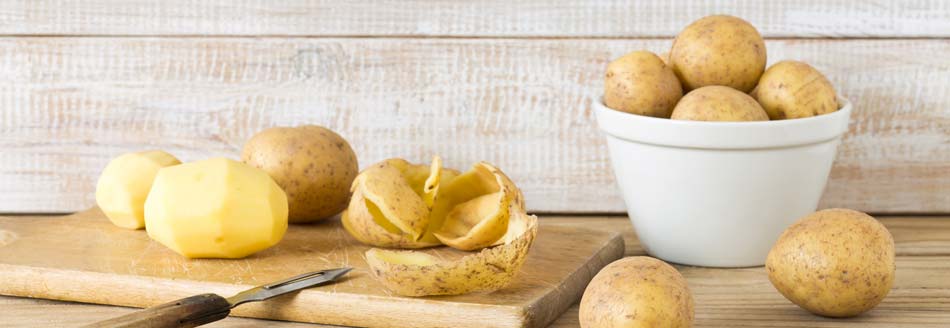 Darf man Kartoffelschalen essen? Kartoffeln liegen z. T. geschält auf einem Holzbrett