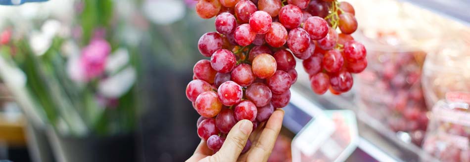 Naschen im Supermarkt: Eine Frau hält frische, rote Trauben im Supermarkt hoch
