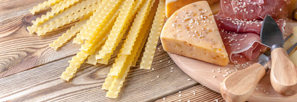 Mafaldine liegen neben Käse und Speck auf Holz
