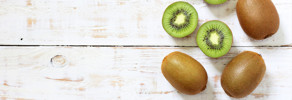 Kiwi mit Schale essen: Ganze und halbe Kiwis liegen auf Holz