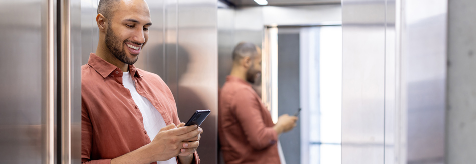 Warum ist häufig ein Spiegel im Aufzug? Ein Mann steht im Fahrstuhl vorm Spiegel und sieht auf sein Handy.