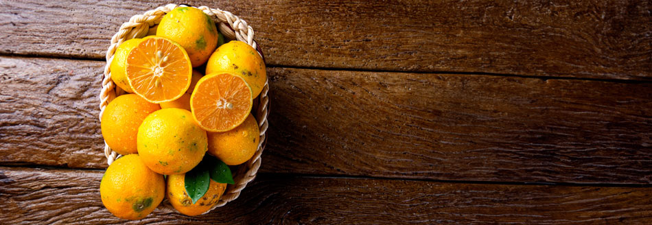 Mehrere orangefarbene Rangpurs liegen in enem Korb, der auf einer dunklen Holzfläche steht.