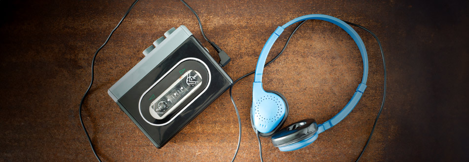 Ein alter Walkman liegt mit angeschlossenen Kopfhörern auf einem braunen Untergrund.