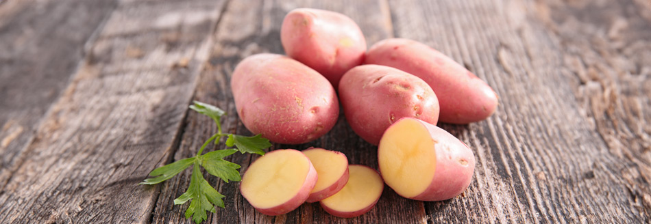 Fünf rote Kartoffeln liegen auf einer Holzfläche. Eine von ihnen ist aufgeschnitten.