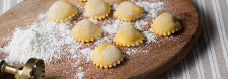 Ungekochte Anolini liegen vorbereitet auf einem Holzbrett.