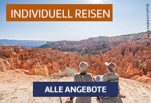 Zwei Personen blicken von einer Felsklippe in eine weite, rot-goldene Canyonlandschaft.