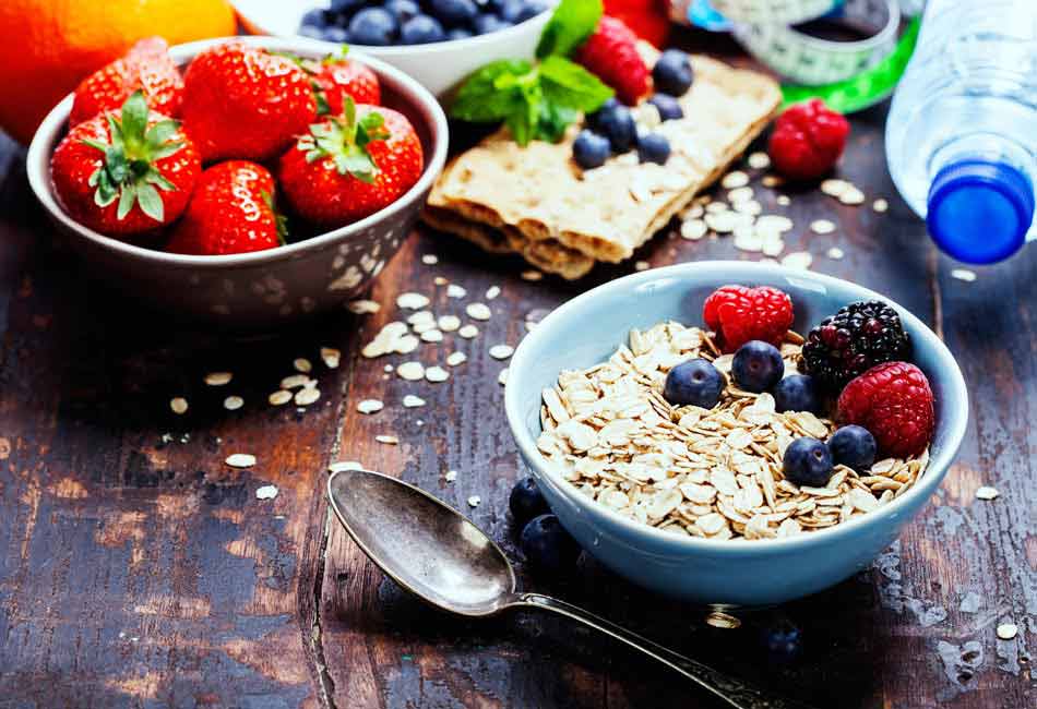 Eine Schale mit Müsli und Beeren steht neben einer Schale mit Erdbeeren