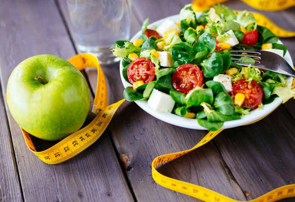 Ein Apfel liegt neben einem Salat. Um beides ist los ein Maßband geschlungen.