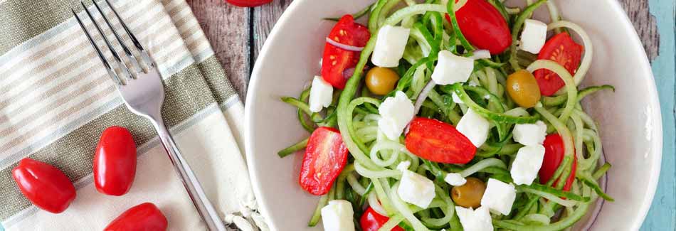 Ein Teller mit Zucchini-Nudeln, Tomaten und Mozzarella steht auf einem Tisch