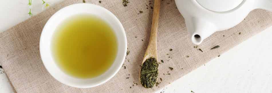 Eine Teekanne mit grünem Tee steht neben einer Tasse