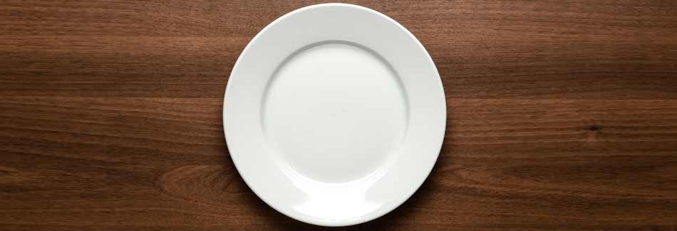 Tisch richtig decken: Ein weißer Teller steht auf einem dunklen Tisch