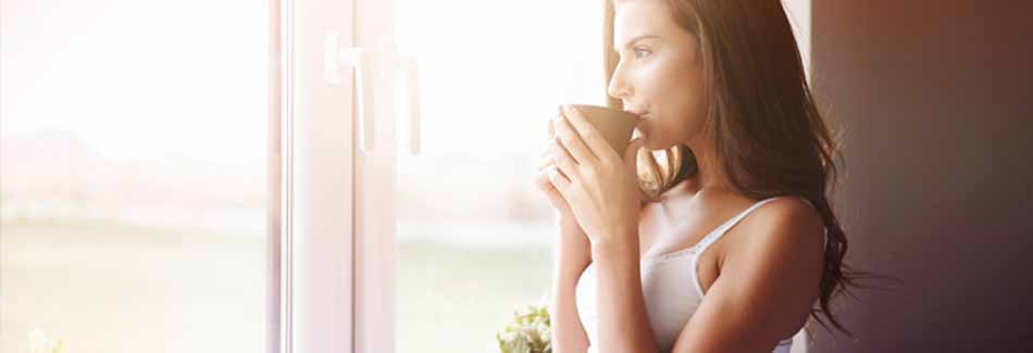 10 Tipps für Morgenmuffel: Eine Frau trinkt Kaffee am Fenster